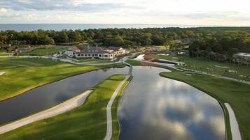 Ein Golfplatz mit Teich, Clubhaus und umliegender Bepflanzung.