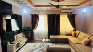Una sala de estar con sofá, televisor, ventilador de techo y alfombra con diseño de mármol.