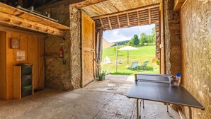 A rustic wooden room with a ping pong table, a fire extinguisher, and a view of a grassy outdoor area with a tent and chairs. - The Bear Fountain (LA FECLAZ LES DESERTS)