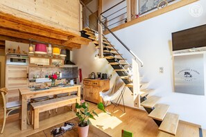 A modern kitchen with wooden cabinetry, a dining area with a wooden table and chairs, and a staircase with a metal railing. - The Bear Fountain (LA FECLAZ LES DESERTS)