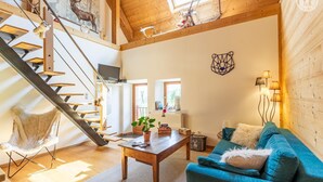 A spacious living area with a wooden staircase, a blue sofa, a coffee table, and a view of the outdoors. - The Bear Fountain (LA FECLAZ LES DESERTS)