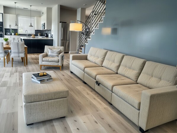 A modern living room with a sofa, ottoman, and a dining area with chairs and a table.