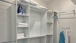Une salle de bain moderne et blanche, dotée d’une douche à l’italienne, d’un porte-serviettes et de serviettes soigneusement pliées, rangées sur des étagères.