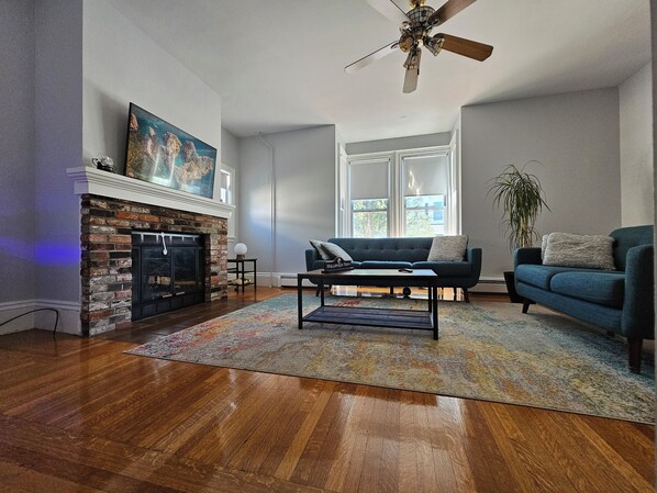 A living room with a fireplace, a sofa, a coffee table, and a large window.