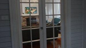 A white-framed door with glass panels, leading to a living room with a fireplace, a couch, and a television.