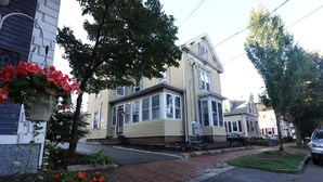 A two-story house with a brick driveway and a front yard with flowers.