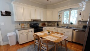 A kitchen with white cabinets, a wooden dining table, and a stainless steel dishwasher.