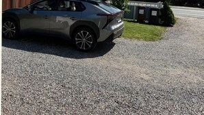 A modern car parked on a gravel driveway with a street lamp and trees in the background.