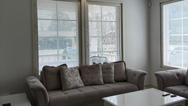 A modern living room with a sectional sofa, a white coffee table, and large windows with blinds.