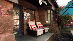 A stone building with a porch, two chairs with cushions, a table, and a blue awning with flowers. - Charming 2-bedroom house, Downtown Flagstaff with AC (Flagstaff)
