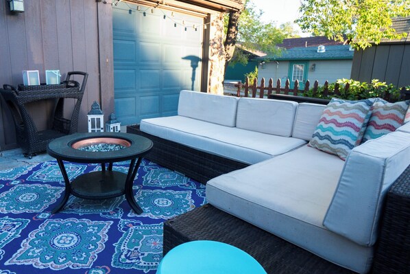 A patio with a white sofa, a round table, and a patterned rug.