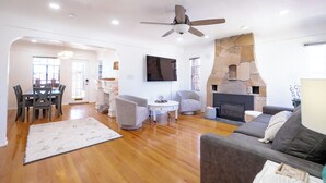 A spacious living area with a fireplace, a ceiling fan, and a dining area with a table and chairs. - Charming 2-bedroom house, Downtown Flagstaff with AC (Flagstaff)