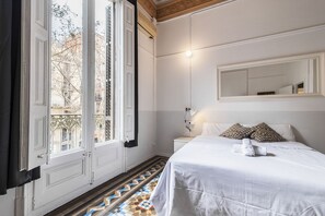 A hotel room with a bed, a bedside table, a mirror, and a window with a view of buildings. - Modernist apartment with AC in central Barcelona! (Barcelona)