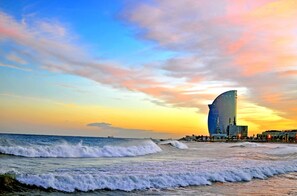 Paisagem costeira urbana com um arranha-céu curvo imponente, ondas se aproximando da costa e um céu ao pôr do sol.