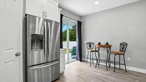 A modern kitchen with a stainless steel refrigerator, white cabinetry, and a sliding glass door leading to a balcony. - Entire New Home w/1 King, 3 Queen beds and Fenced backyard (Bonita Springs)