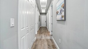 A hallway with white doors, a wooden floor, and a ceiling light fixture. - Entire New Home w/1 King, 3 Queen beds and Fenced backyard (Bonita Springs)