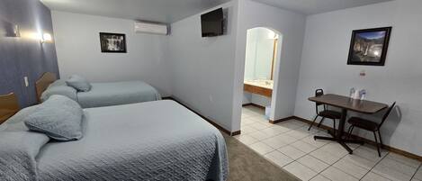 Une chambre d’hôtel avec deux lits, un bureau et une chaise. On y trouve un miroir, une télévision et un tableau encadré au mur.