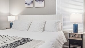 A neatly arranged bedroom with a large bed, two bedside tables, and a window with blinds.