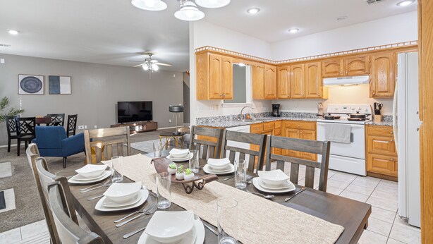 A modern kitchen with wooden cabinets, a white refrigerator, and a dining area with a long table set for six.