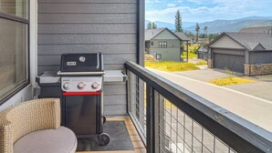 Parvekkeella on grilli, rottinkituoli ja sieltä avautuu näkymä asuinalueelle, jossa on taloja ja vuoria.