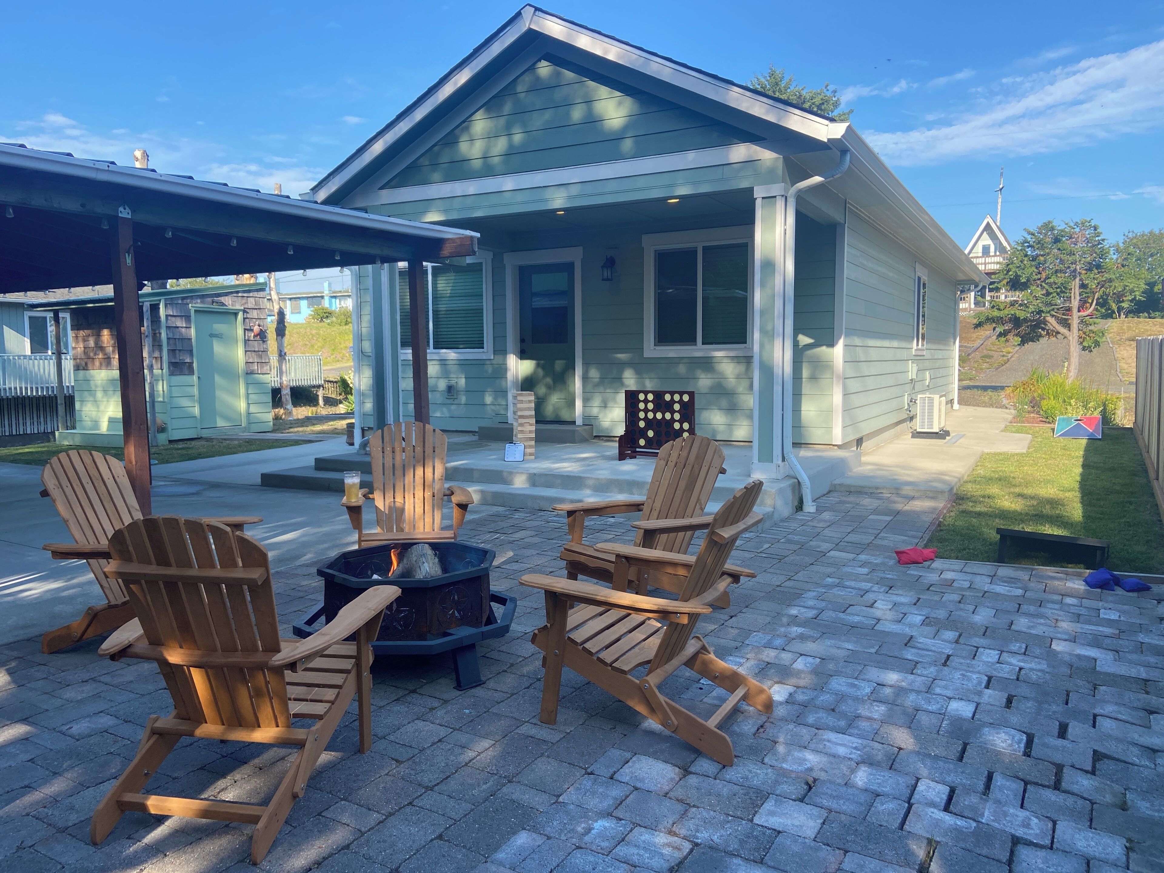 A house with a covered patio area featuring four wooden Adirondack chairs and a fire pit.