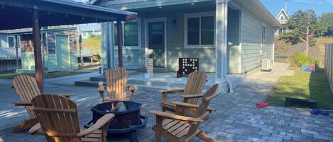 A house with a covered patio area featuring four wooden Adirondack chairs and a fire pit.