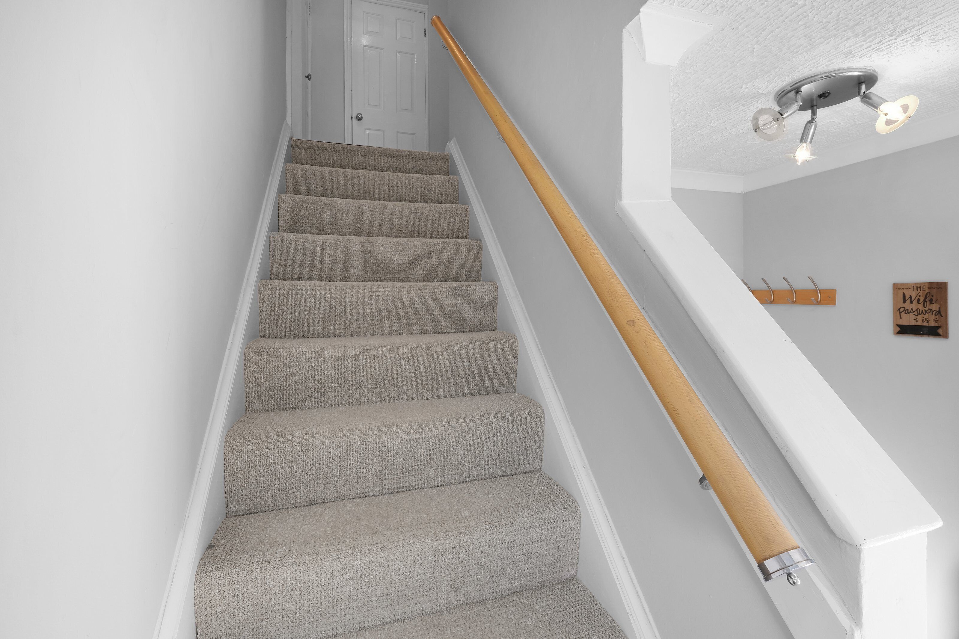 A staircase with carpeted steps and a wooden handrail, leading to a white door.