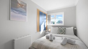 Quarto com cama, mesa de cabeceira, janela e radiador.