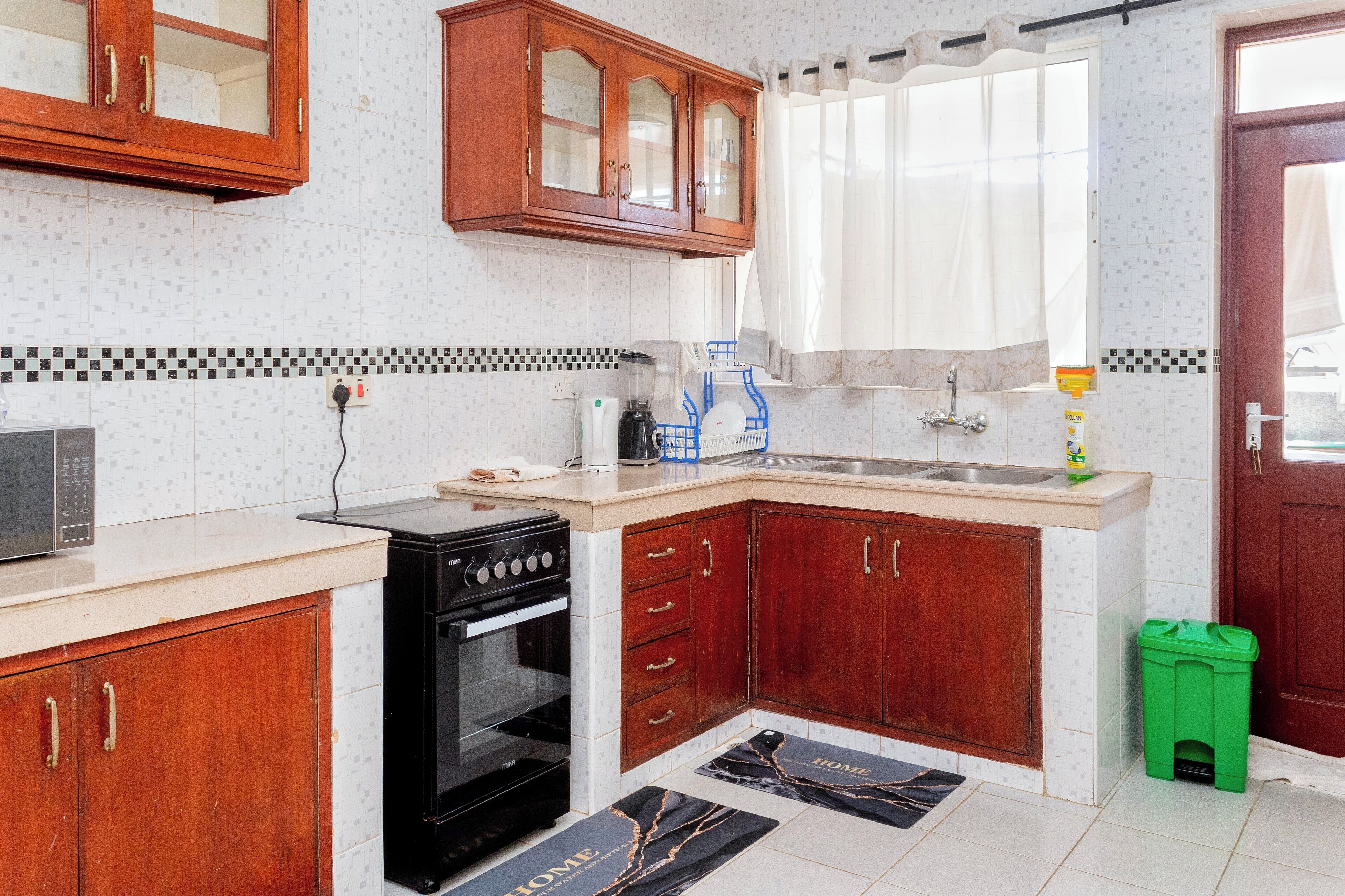 Una cocina con armarios de madera, estufa negra, un lavamanos y un cubo de basura verde.