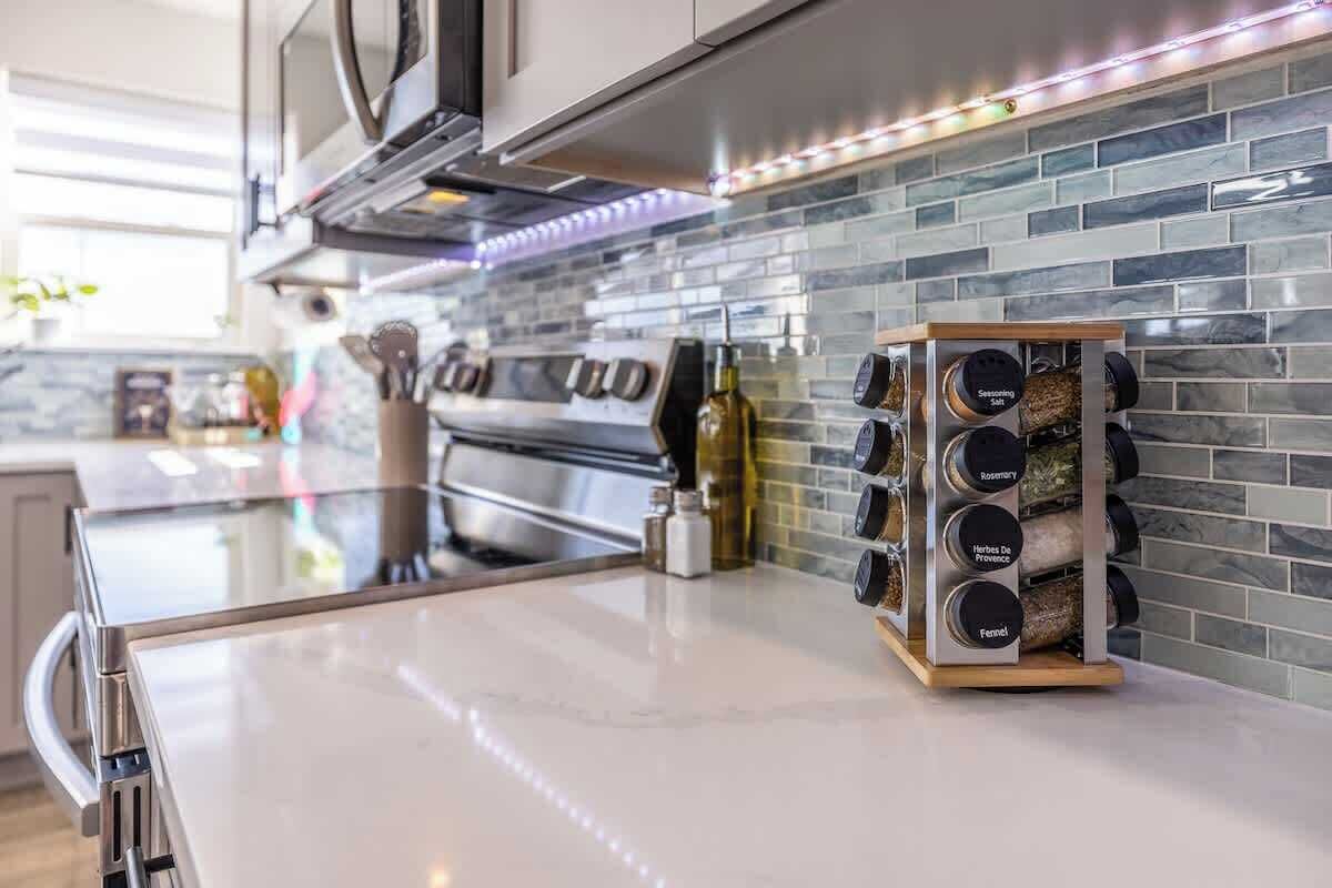 Una cocina moderna con horno de acero inoxidable, microondas integrado y especiero con recipientes etiquetados.
