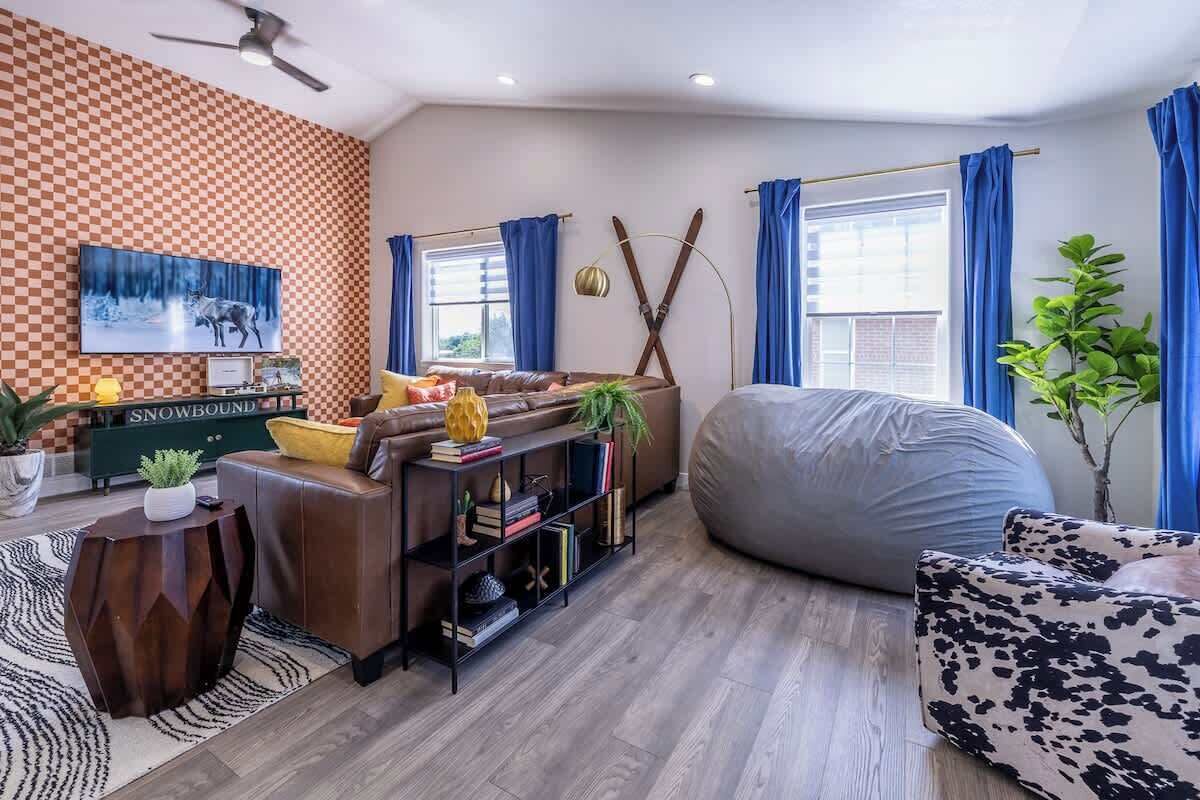 A modern living room with a checkered wall, a sofa, a bean bag, a bookshelf, and a television.