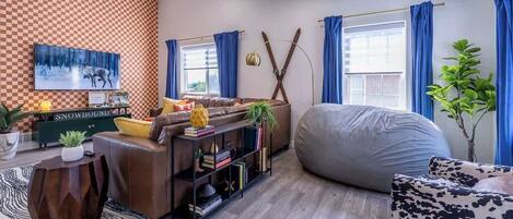 A modern living room with a checkered wall, a sofa, a bean bag, a bookshelf, and a television.