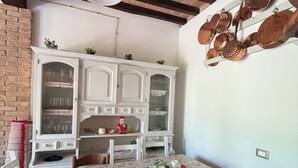 A dining area with a table covered by a floral tablecloth, wooden chairs, a white cabinet with glass doors, and a hanging copper pot rack. - Shelter among olive trees, Tuscan countryside, a stone's throw from characteristic cities (Toscana)