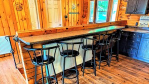A wooden interior with a bar area featuring stools and a counter. - Beautiful Log Home + XL BUNKIE by Weslmkoon lake (Denbigh)