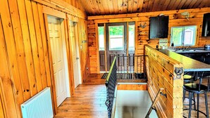 A cabin interior with wooden walls, a kitchen area, and a staircase leading to a loft. - Beautiful Log Home + XL BUNKIE by Weslmkoon lake (Denbigh)