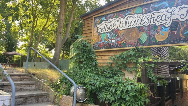 A wooden building with a mural sign reading "The Wheat Shed." - The Wheatsheaf (Newmarket)