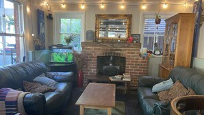 A cozy living room with leather sofas, a wooden coffee table, a fireplace, and string lights. - The Wheatsheaf (Newmarket)