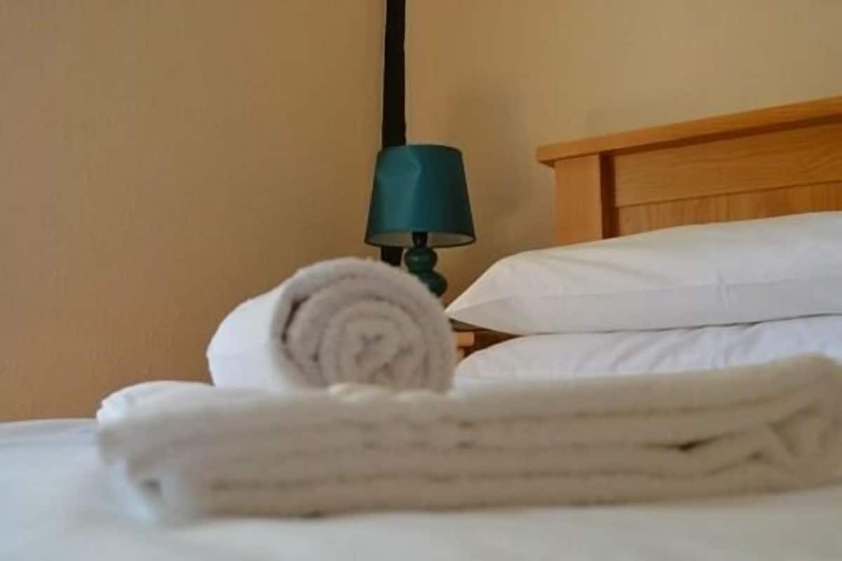 A neatly made bed with white linens and a rolled towel on the side.