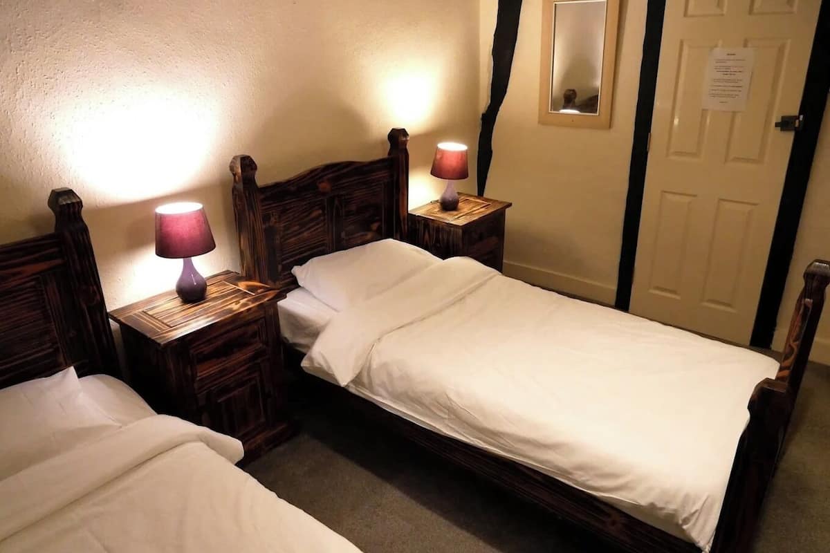 A double room with two wooden beds, each with a nightstand and a lamp.