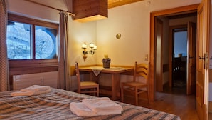 A cozy room with a bed, a table with chairs, and a window with curtains.