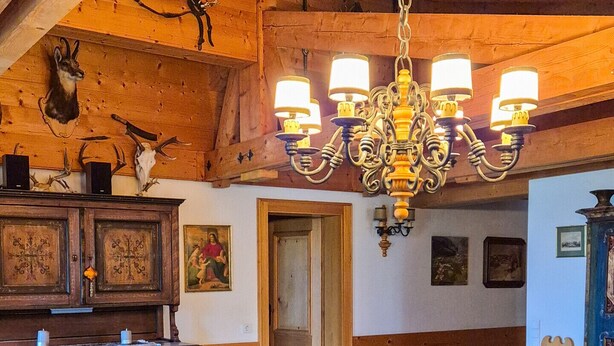 A cozy living room with a wooden ceiling, a chandelier, a fireplace, and a sofa set.