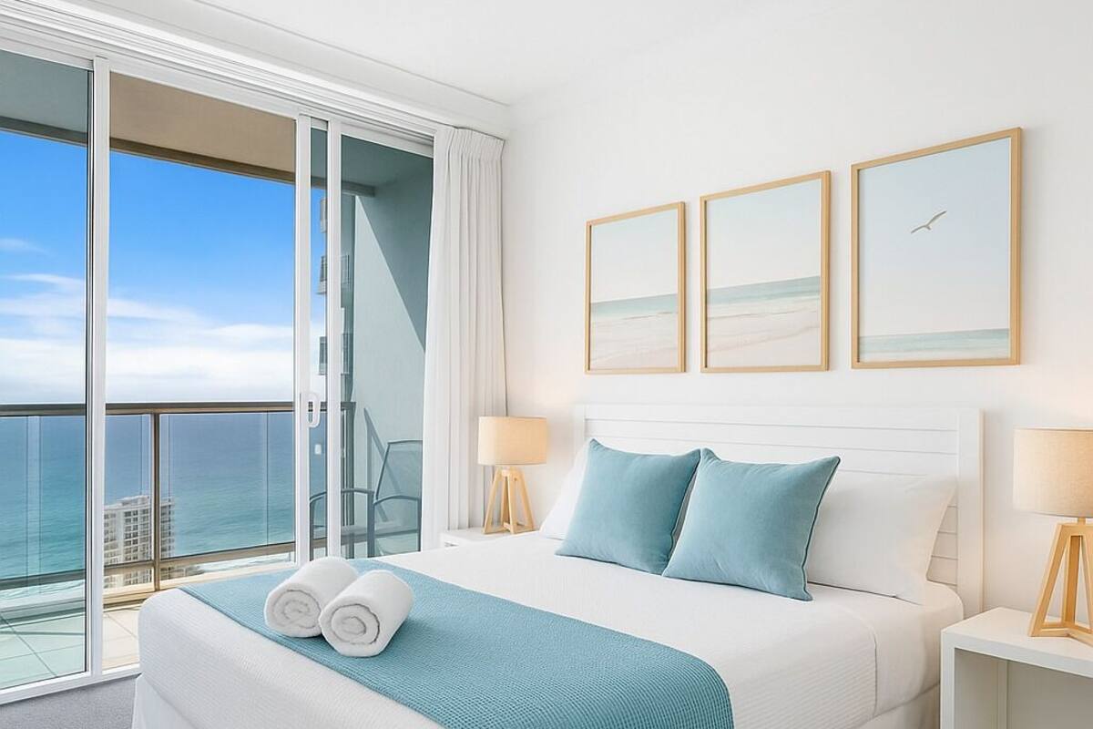 A hotel room with a large bed, two bedside tables, a view of the ocean, and three framed pictures on the wall.