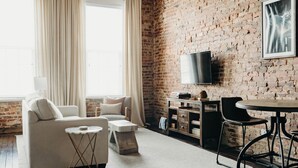 Een woonkamer met een bakstenen muur, een bank, een salontafel, een televisie en een eettafel.