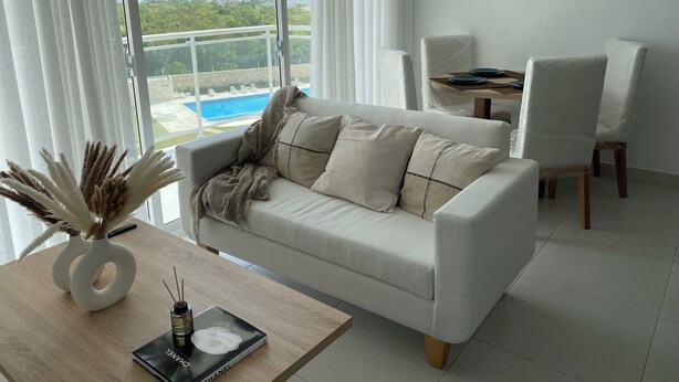 Un salón moderno con un sofá blanco, una mesa de centro de madera y vistas a una piscina a través de amplios ventanales.