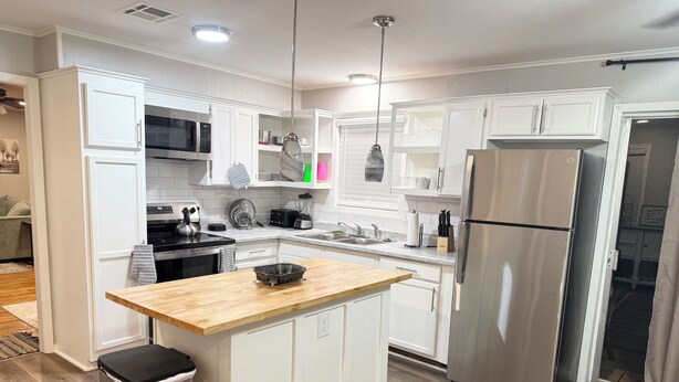 A modern kitchen with white cabinetry, stainless steel appliances, and a wooden countertop.