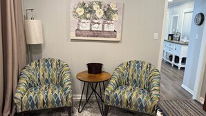 A room with two patterned armchairs, a small round table, and a painting on the wall.