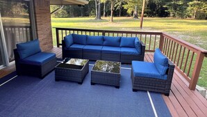 A deck with a blue outdoor sofa, two side tables, and a glass door leading to a covered area.
