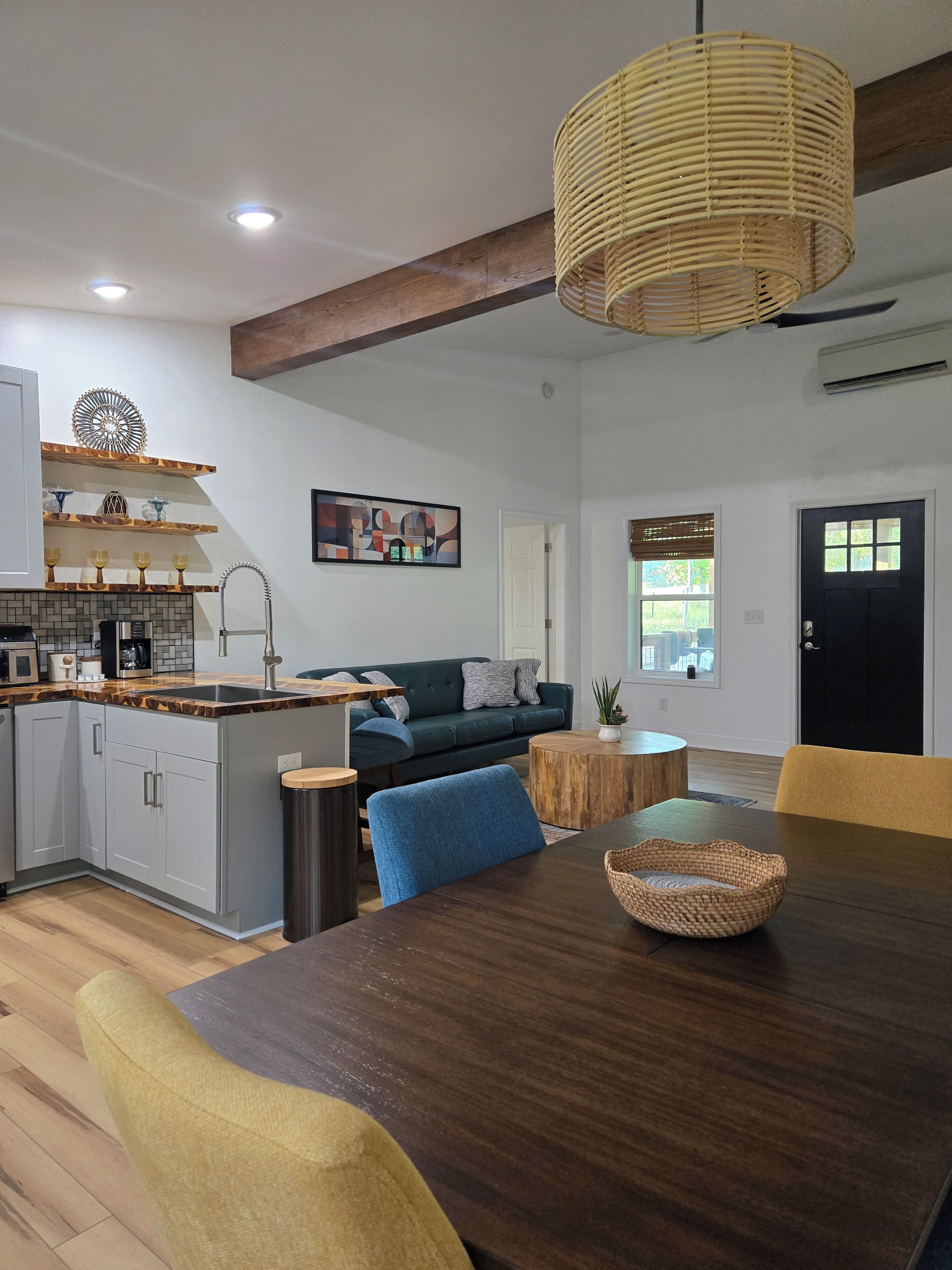 Une cuisine moderne dotée d’un îlot central intégré, un coin repas avec une table en bois et un salon avec un canapé et un tableau au mur.