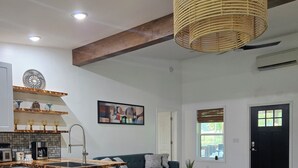 A modern kitchen with a built-in island, a dining area with a wooden table, and a living room with a sofa and a painting on the wall.