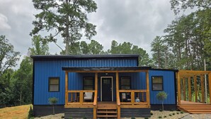 A blue cabin with a wooden porch, a front door, and a small front yard with a stone pathway.
